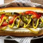 Close-Up Of A Gourmet Hotdog With Fresh Toppings On Wooden Surface.