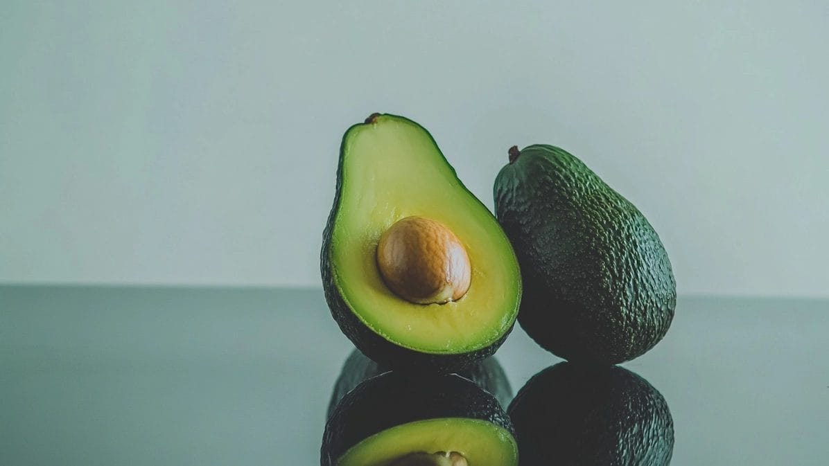 Close-Up Of Halved And Whole Avocados On Reflective Surface