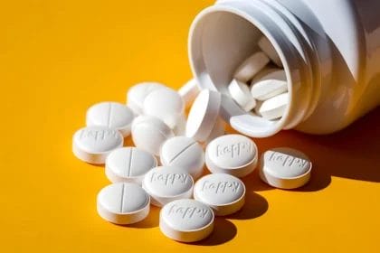 White Pills Labeled 'Happy' Spilling From A Bottle On Yellow Background.