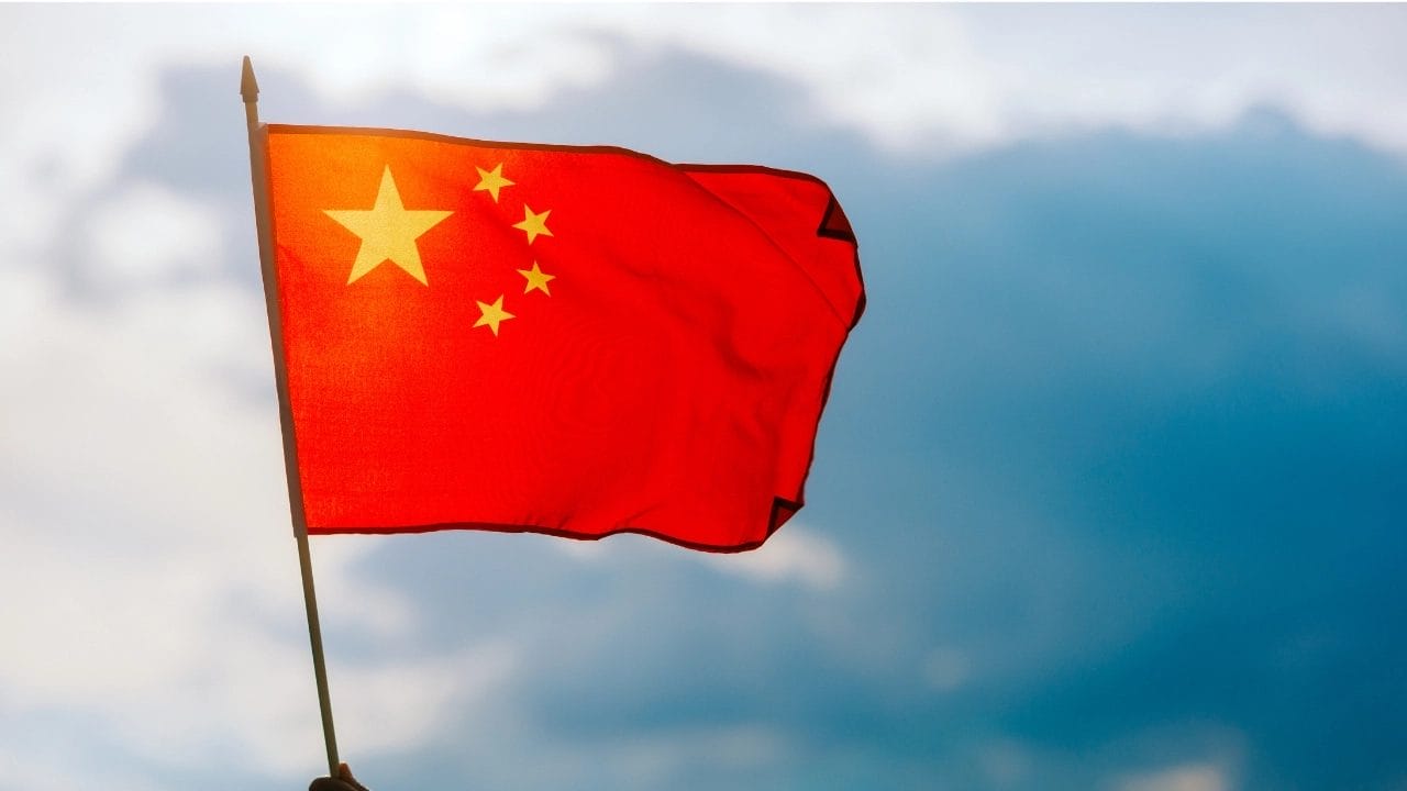 Individual Displaying The China Flag Under A Bright Blue Sky