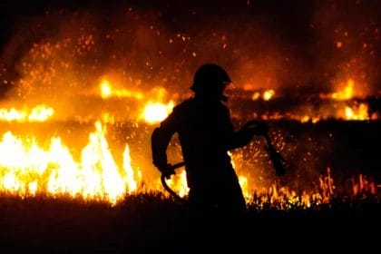 Silhouette Of A Firefighter In Front Of A Large Bonfire.