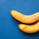 Two Ripe Bananas With Brown Spots On A Blue Background.