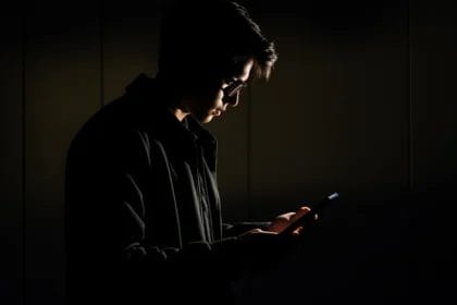 Young Man With Glasses, Illuminated By Smartphone Light In Dark Room.